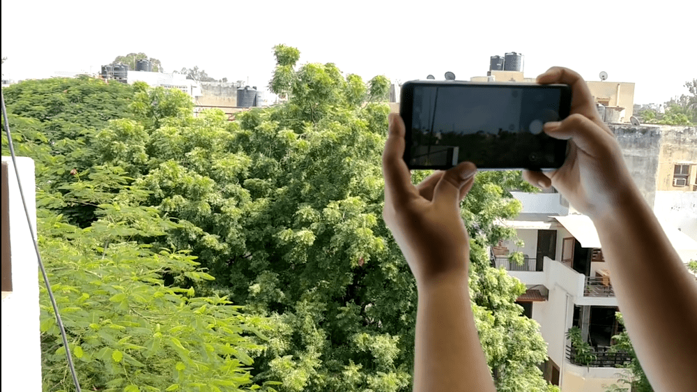 Photo shows a person holding out their smartphone against a landscape of green trees to analyze air quality.