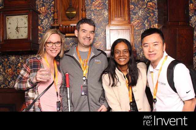 A group of people posing for a picture in a room. I recognize 4 people: Jack, Kanbo, Alak, and Trac. There was text found in the image as well. It reads: AWS re: Invent